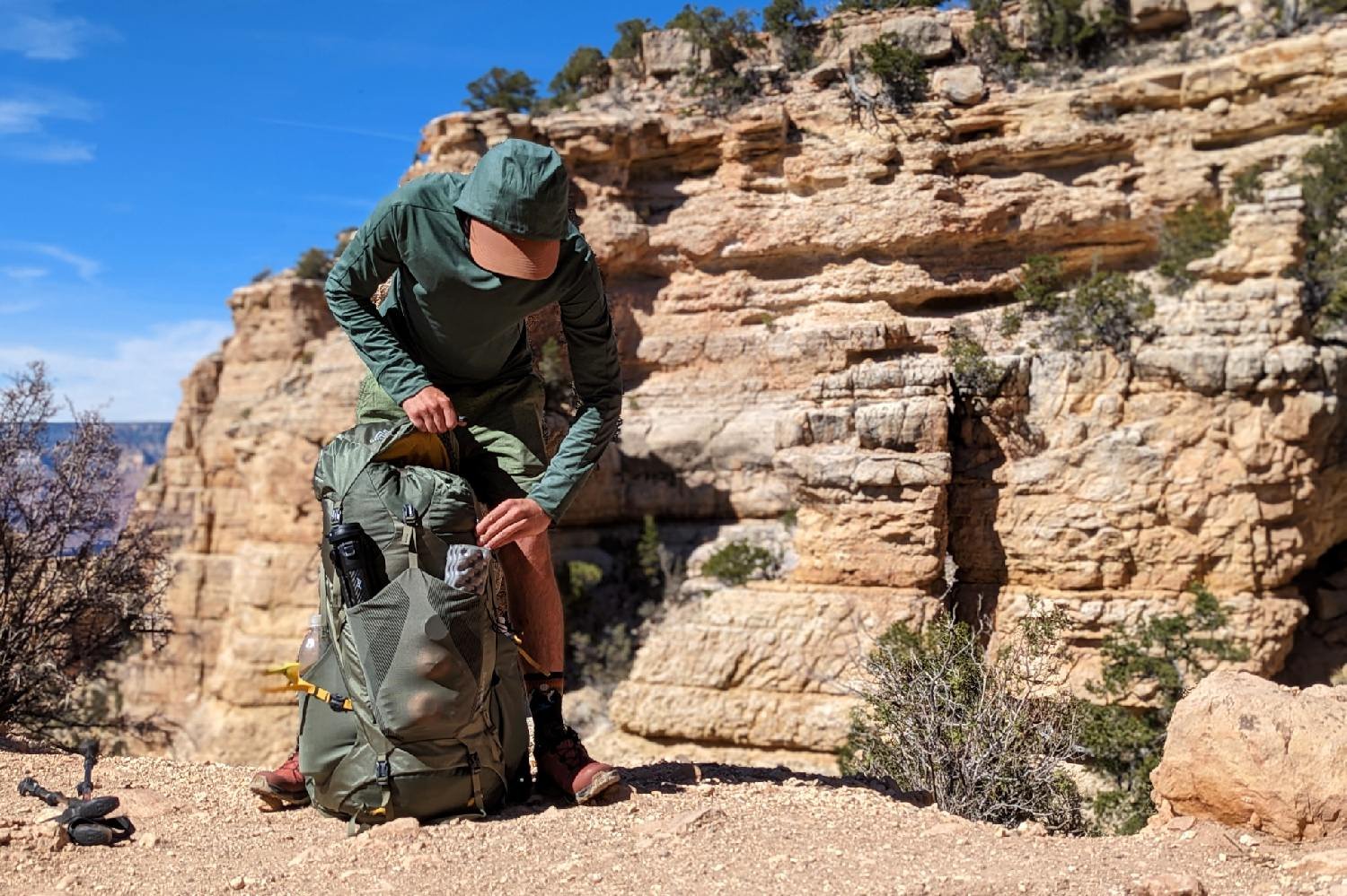 A hiker unclipping the top of lid of the Gregory Paragon 58 backpack with a Grand Canyon view in the background