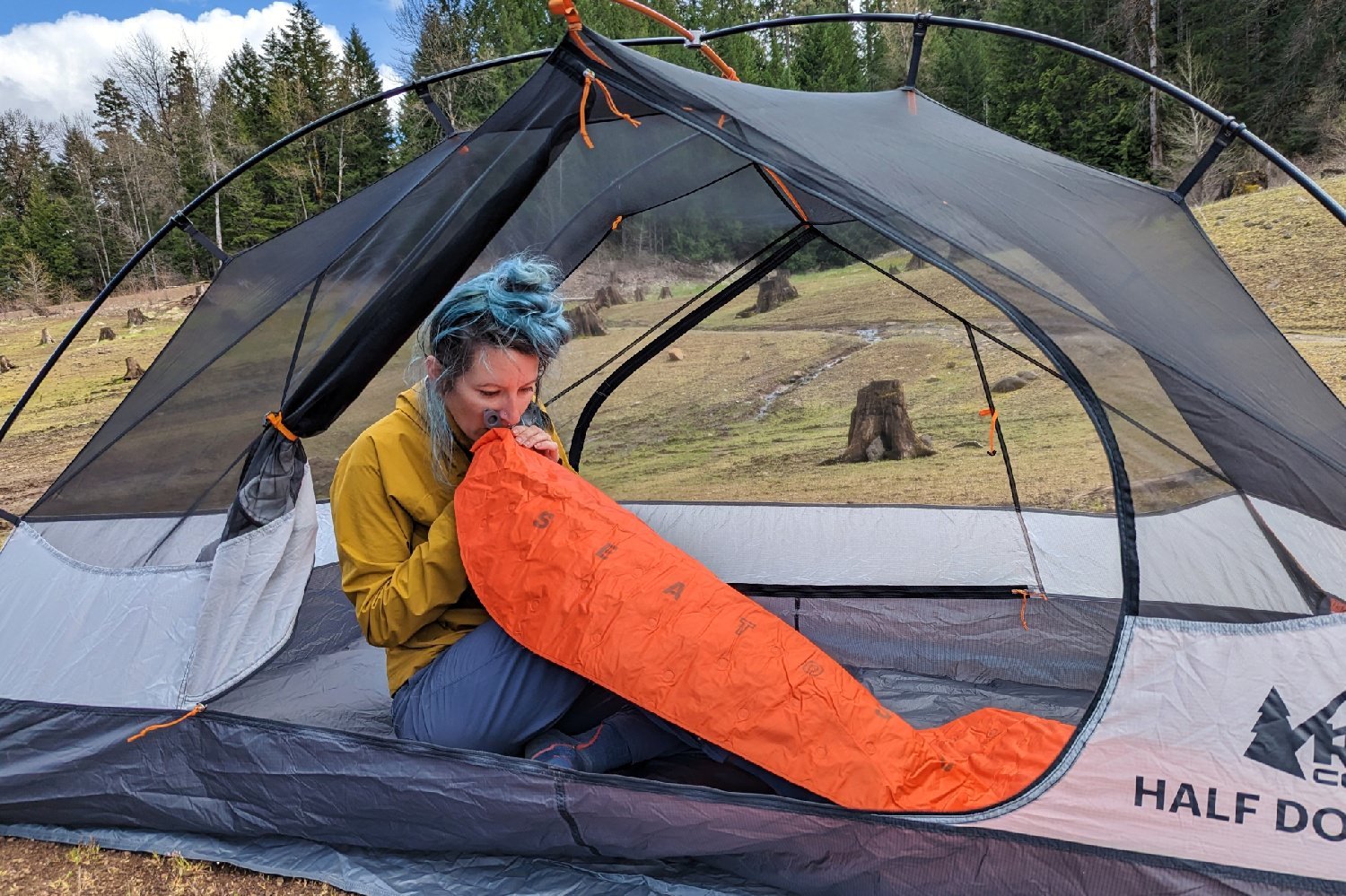 A hiker sitting in the REI Half Dome 2 with the door open - they are blowing up an orange sleeping pad