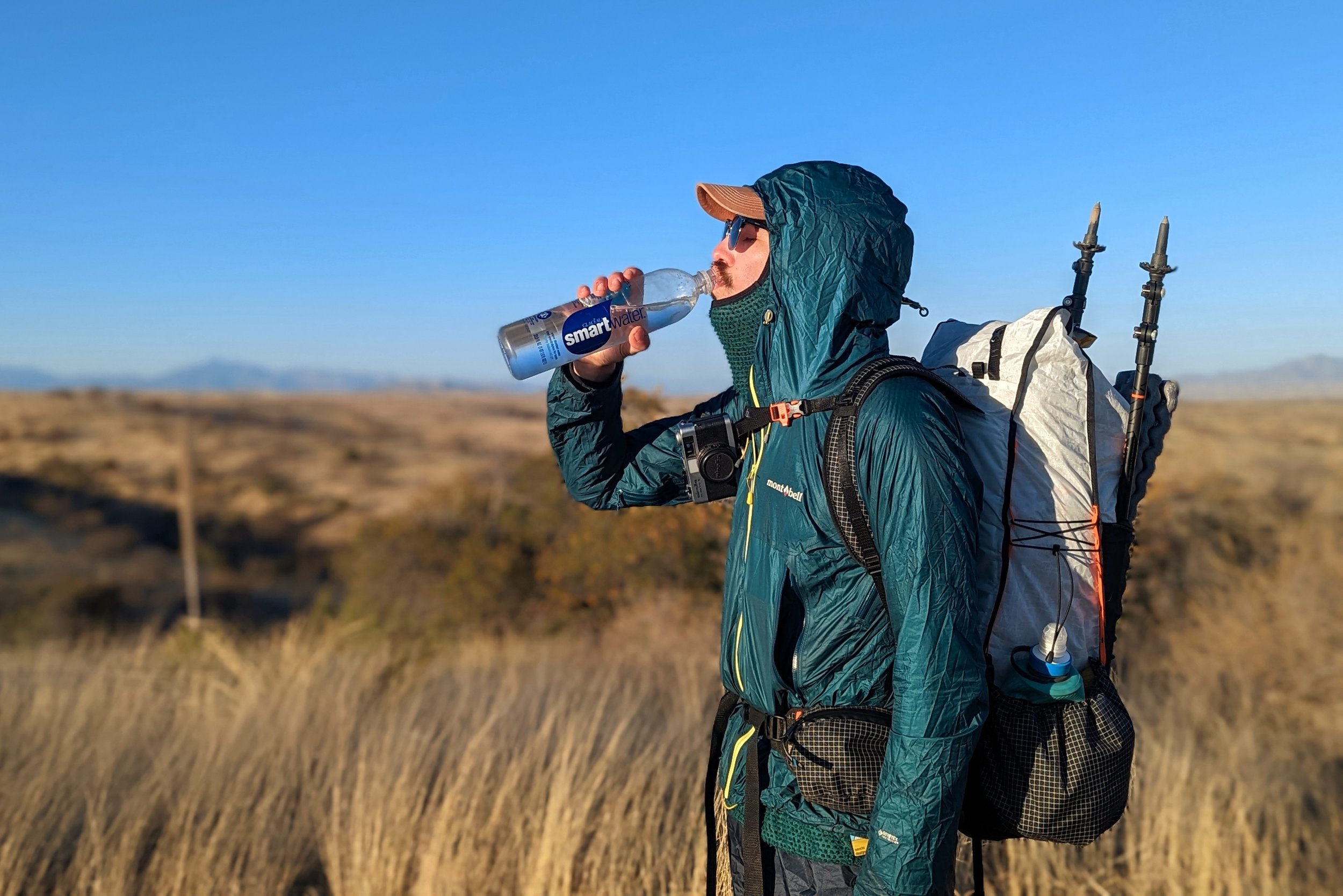 A side view of a hiker wearing the Hyperlite Mountain Gear Unbound 40 drinking from a smartwater bottle in a grassy desert landscape