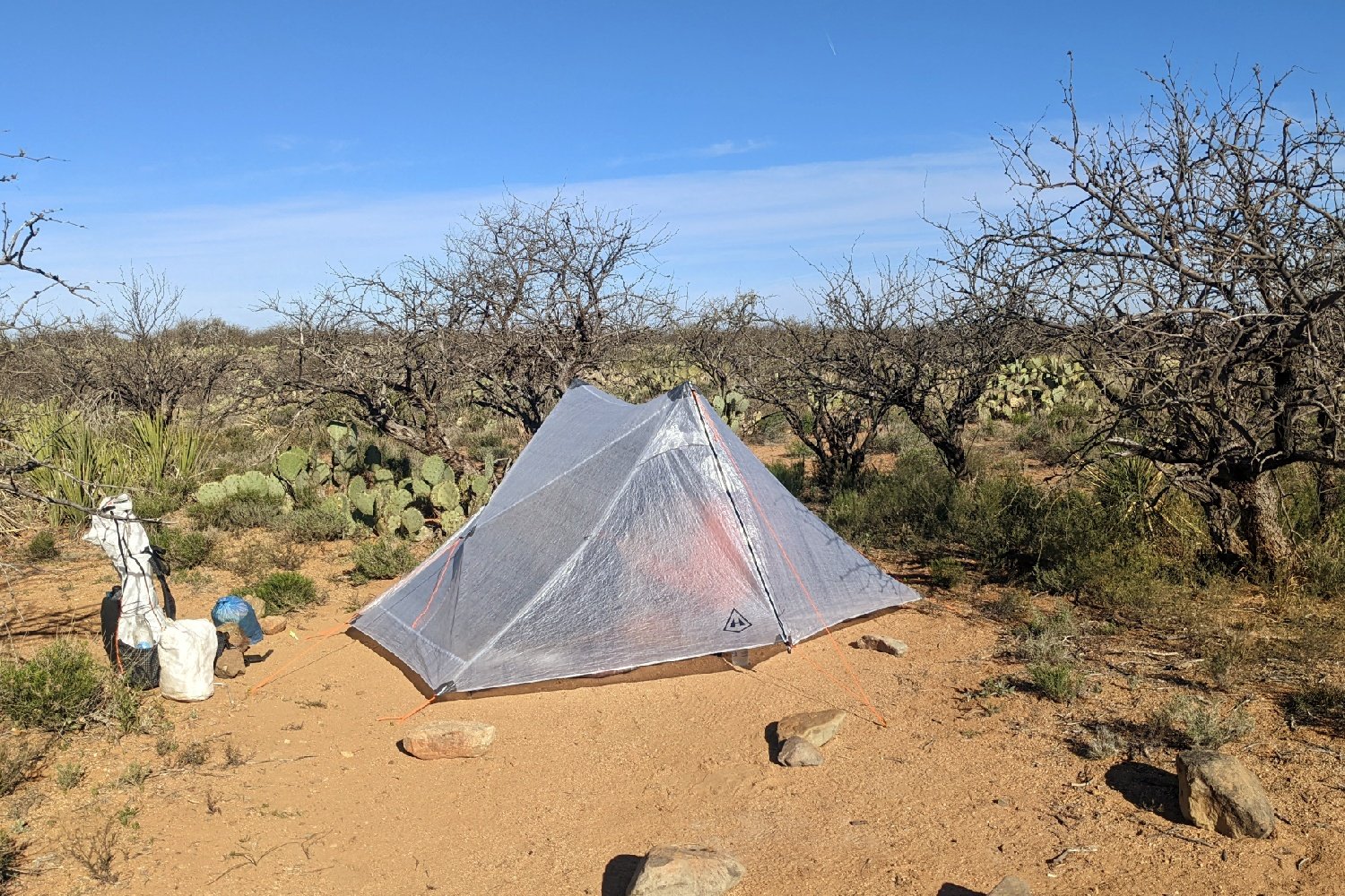 The HMG Unbound 2 pitched taut in a sunny campsite - the fabric is somewhat see-through and there is a hiker sitting inside