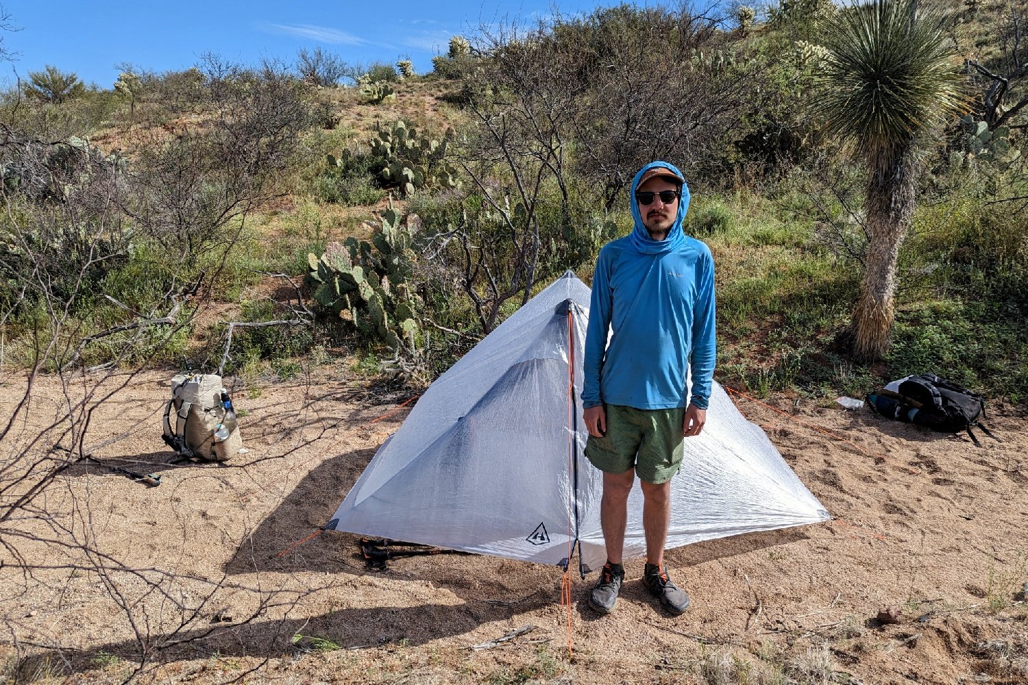 A hiker standing in front of the Hyperlite Unbound two person tent in a deset campsite surrounded by cacti