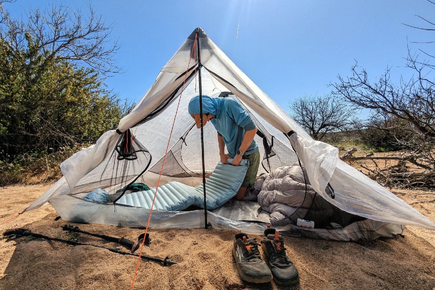 A hiker on his knees in the HMG Unbound 2 rolling up a sleeping pad - the doors and vestibule of the tent are open