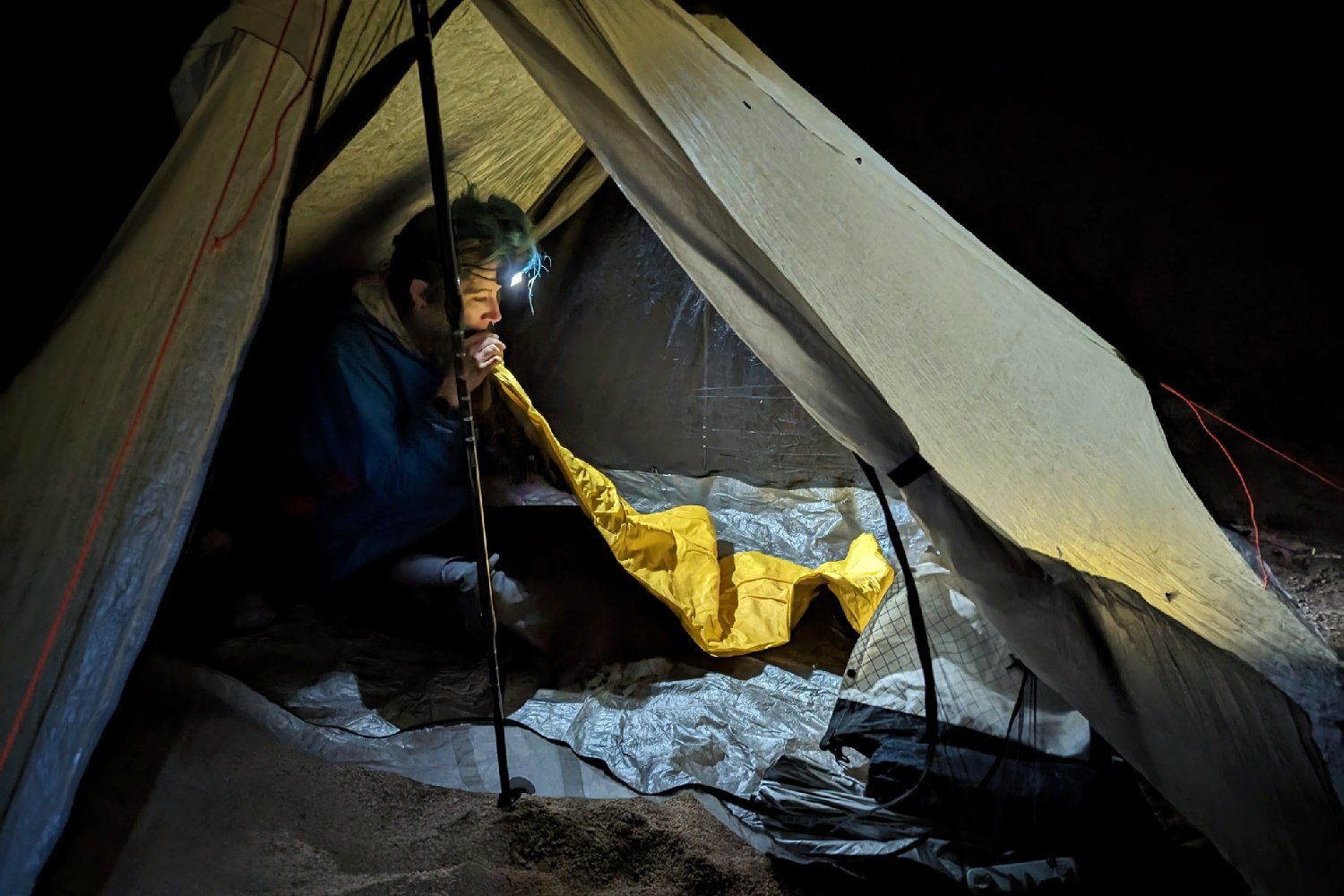 a thru-hiker inside their tent at night inflating their therm-a-rest neo air xlite nxt sleeping pad. The scene is lit up with a headlamp