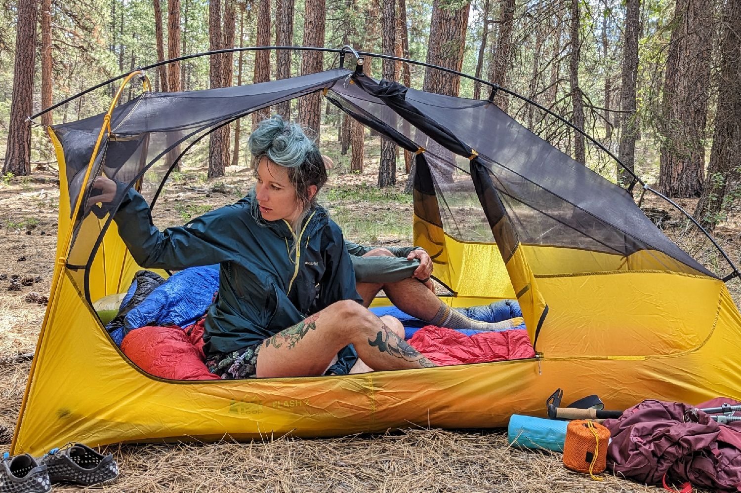 Two hikers sitting in the REI Flash 2 Tent - the view is from the side of tent and the hiker closest in the frame is reaching back to grab something out of the pocket on the headwall