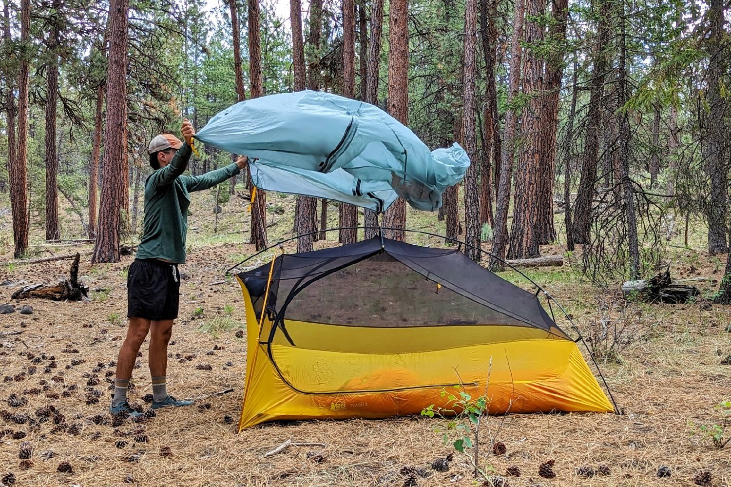 A hiker spreading the rainfly onto the REI Flash 2 Tent in a forested campsite