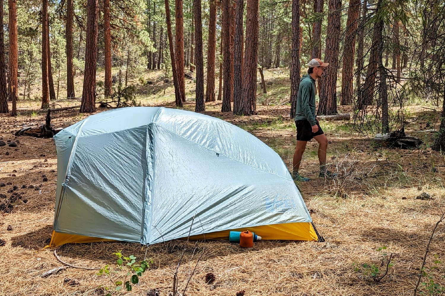 The REI Flash 2 Tent setup with the rainfly on in a forest campsite - a hiker is walking by in the background