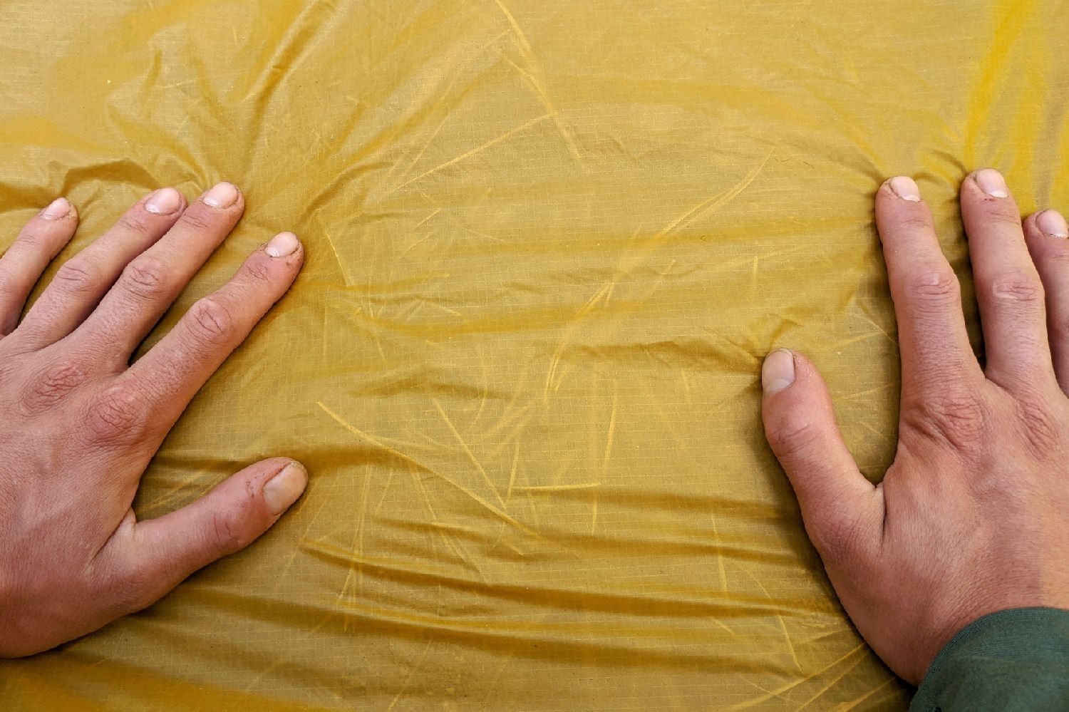 The floor material of the REI Flash 2 Tent being held tight to show that the floor is see-through - several pine needles are visible underneath the floor