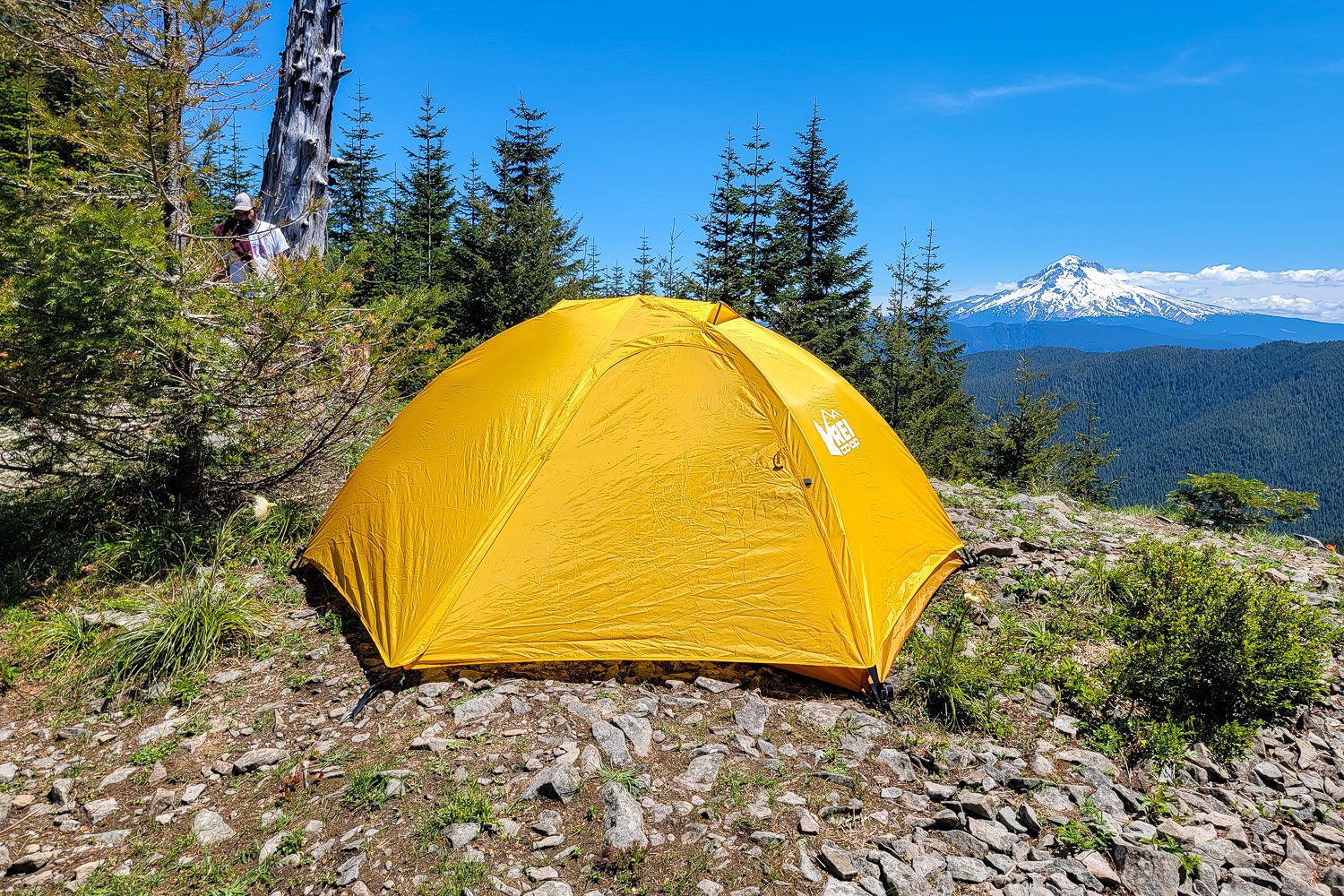 The REI Trailmade 2 tent with its rain fly on pitched on a ridge with a mountain in the background