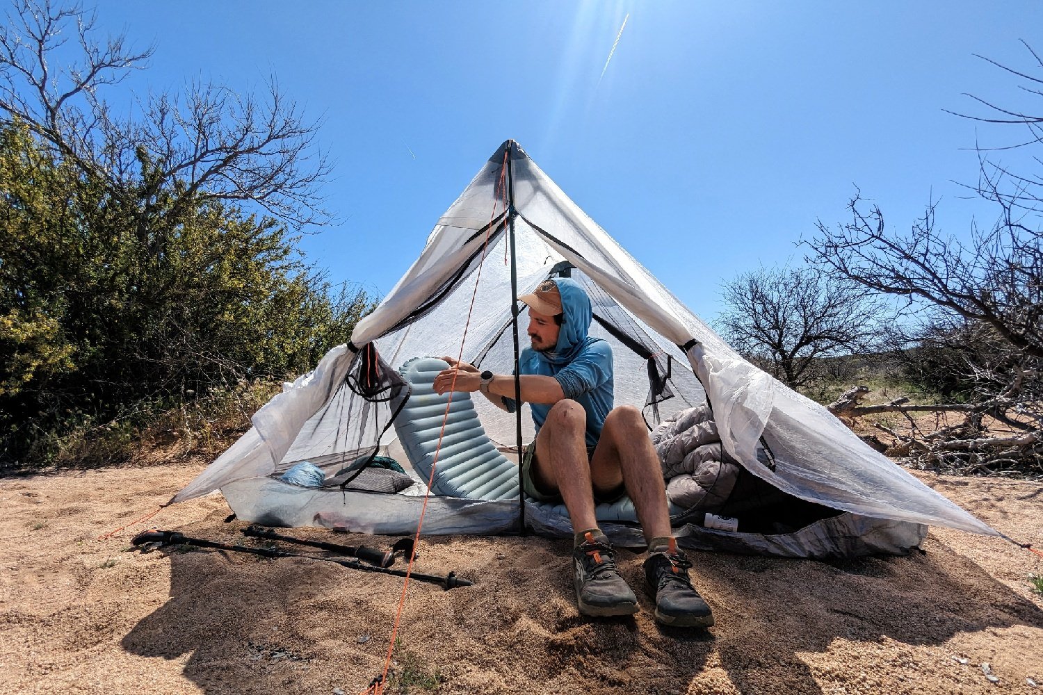 A hiker sitting in a tent in a desert campsite letting some air out of the Therm-a-Rest NeoAir Xtherm NXT to get the right firmness