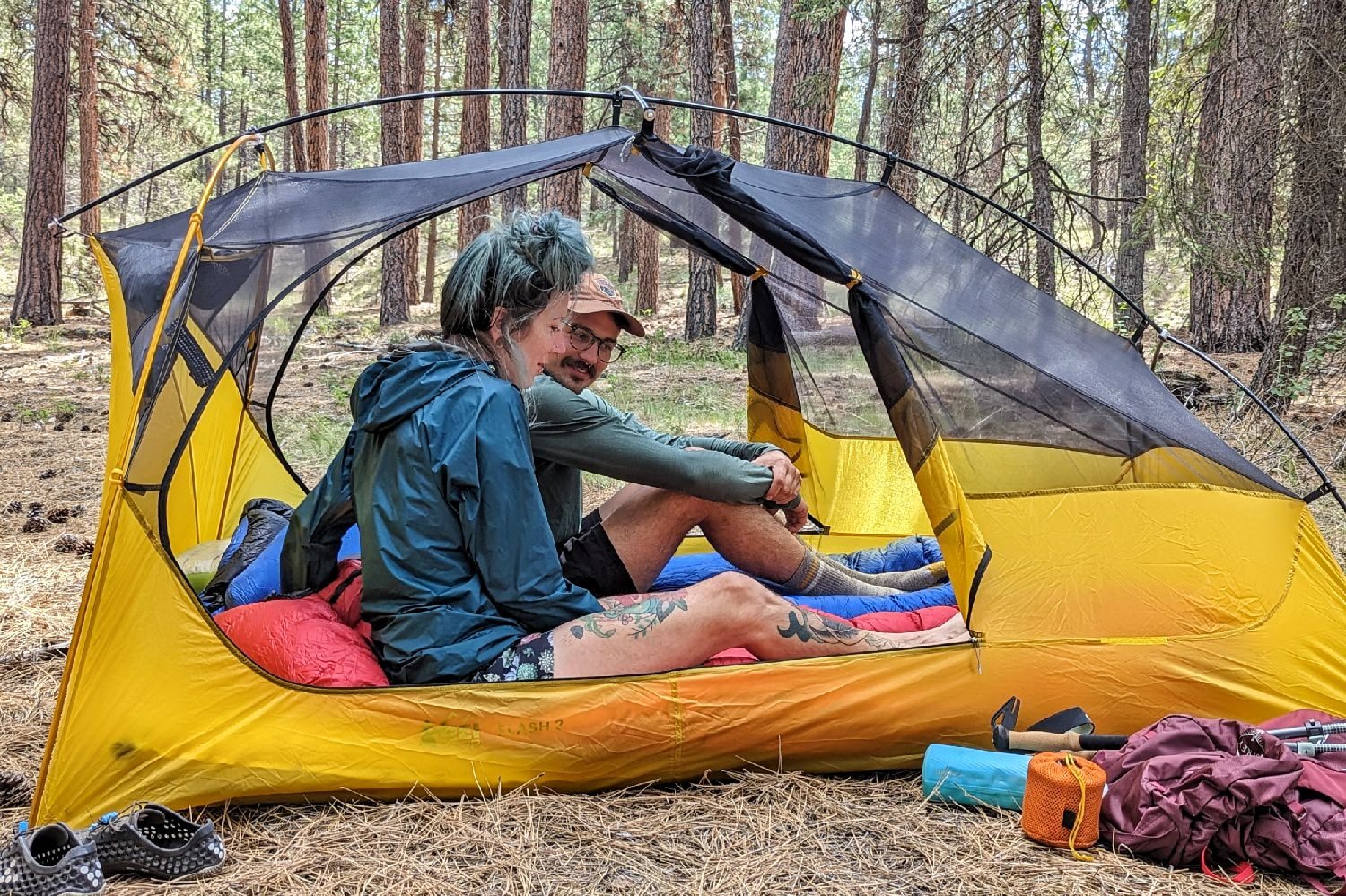 Two hikers sitting in a tent together and talking in a forested campsite
