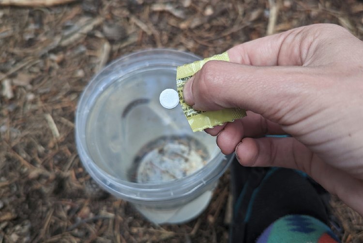 Closeup of a hiker dropping a Katadyn Micropur Tablet into a liter of water