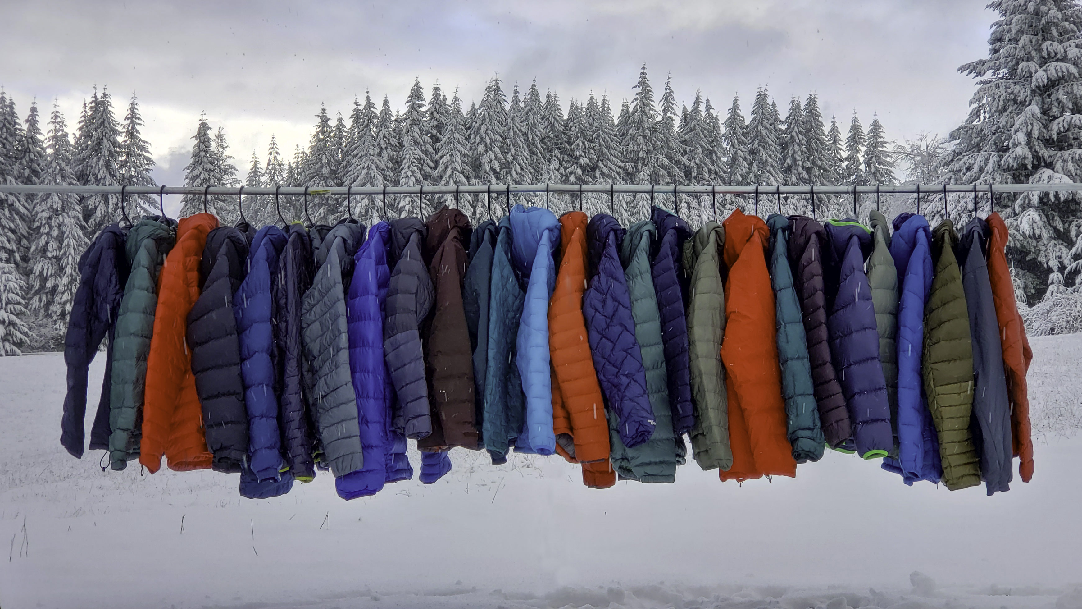 Lots of down jackets on a rod in front of a snowy outdoor scene