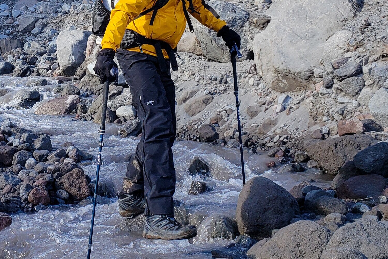 A backpacker crossing a glacial stream in the Arc’teryx Zeta SL rain pants