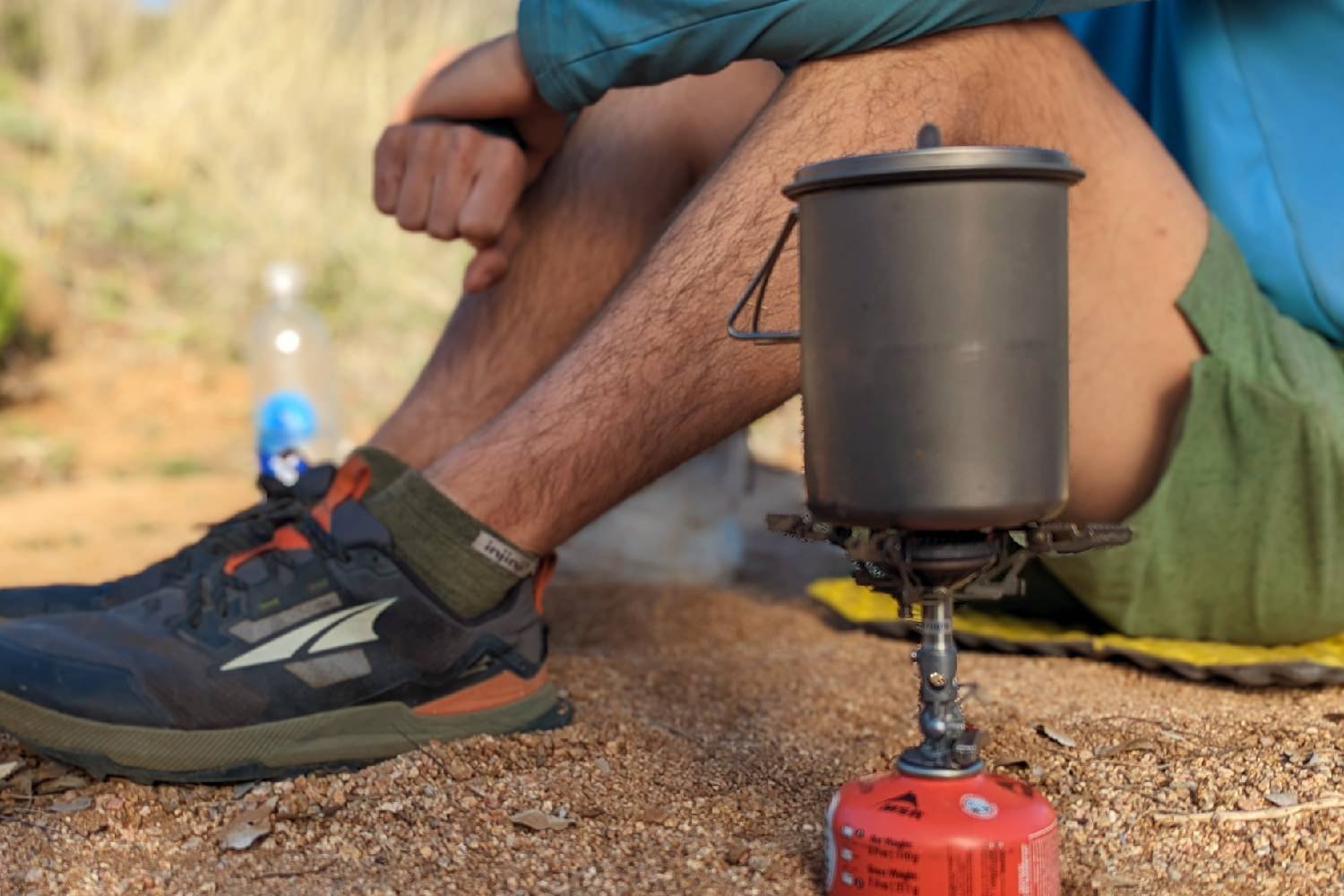 A hiker cooking with the SOTO Windmaster stove in a desert campsite - only the hikers legs and arms are in the frame behind the cookset