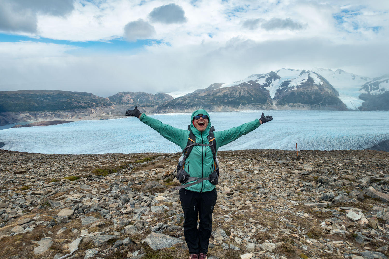 An excited backpacker in a rain jacket in front of a glacier.