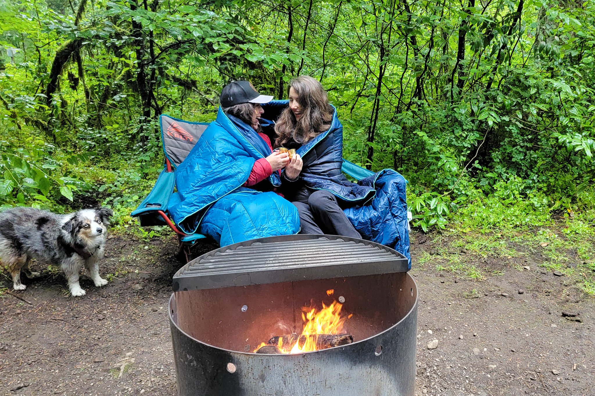 Two women using the Rumpl Original Puffy while sitting around the campfire