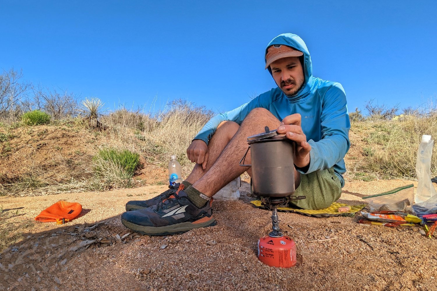 A hiker looking inside a pot that's sitting on the SOTO Windmaster stove - its a desert scene with dried grasses and a vivid blue sky