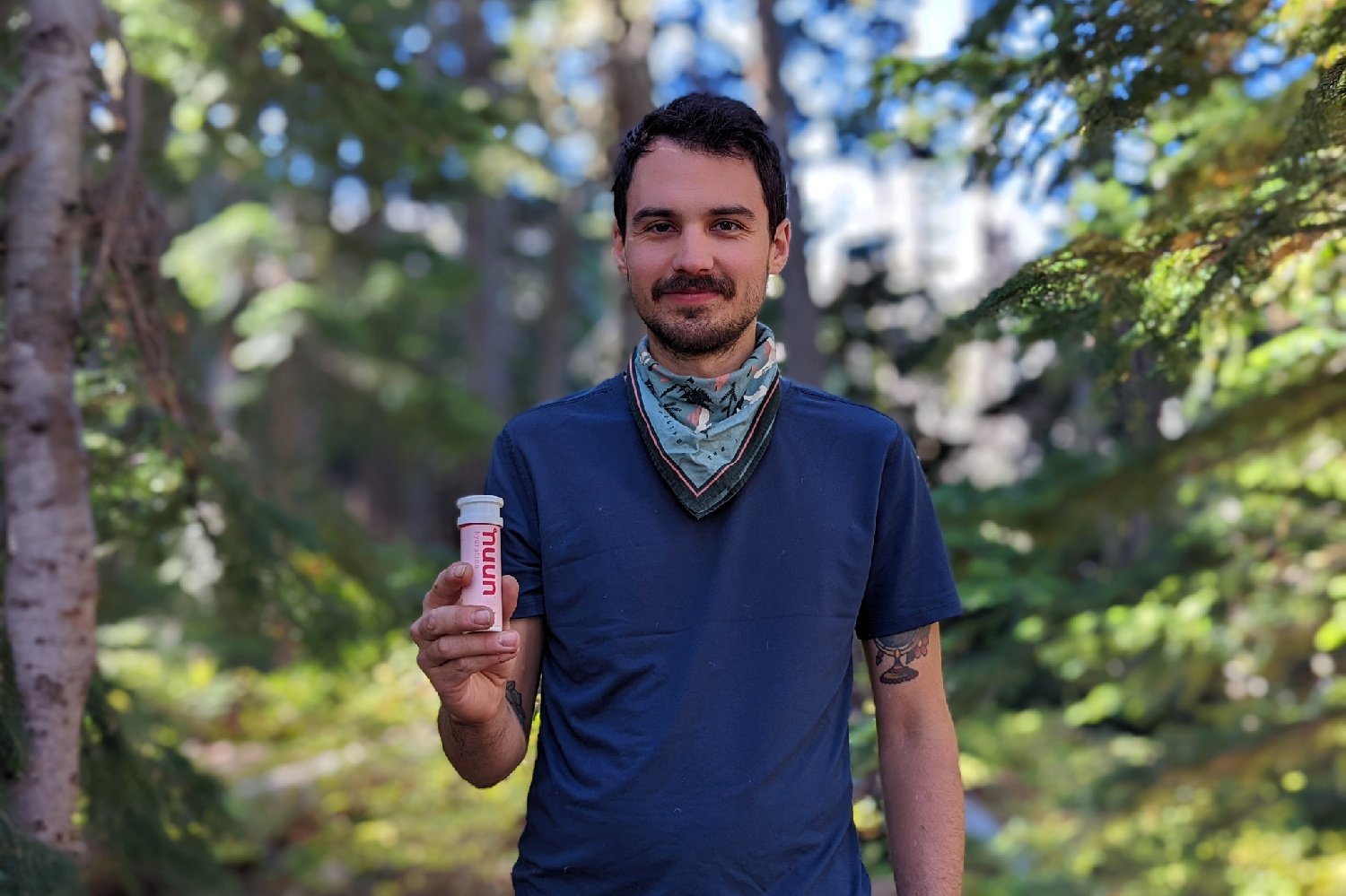 A hiker in a forest holding a bottle of Nuun tablets