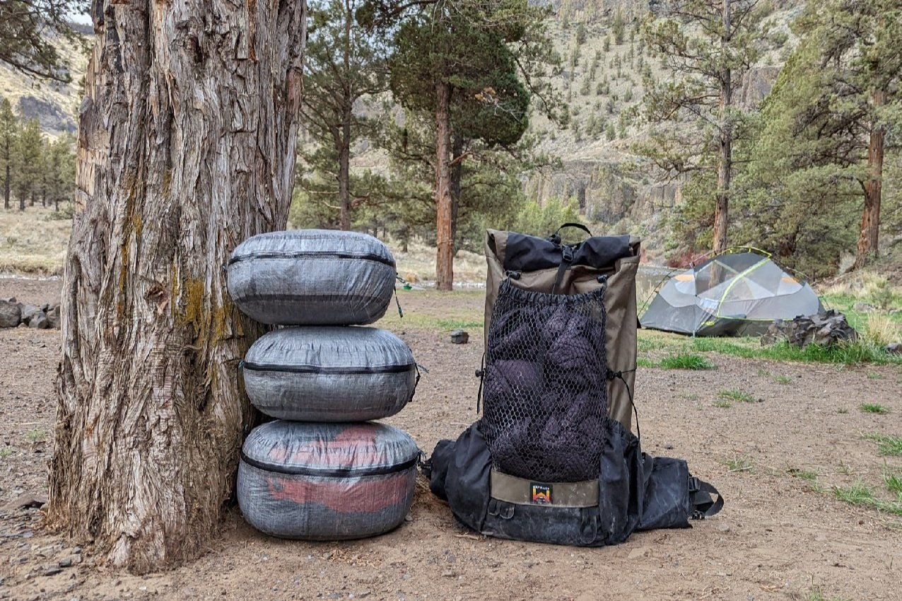 Three Hyperlite Mountain Gear Stuff Pods stacked up next to a backpack at a campsite