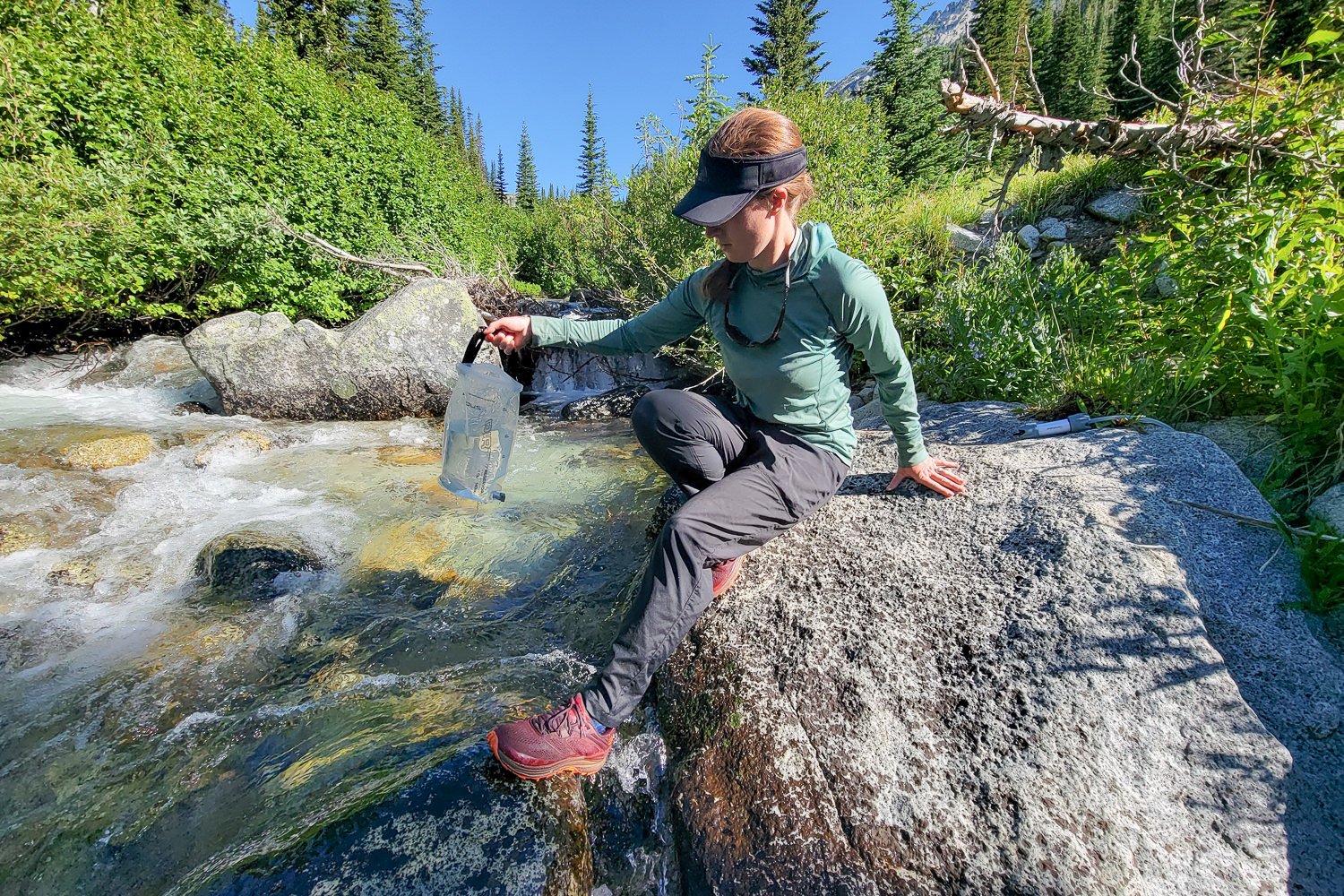 A hiker filling up water from a mountain stream wearing the Mountain Hardwear Trail Sender Pants