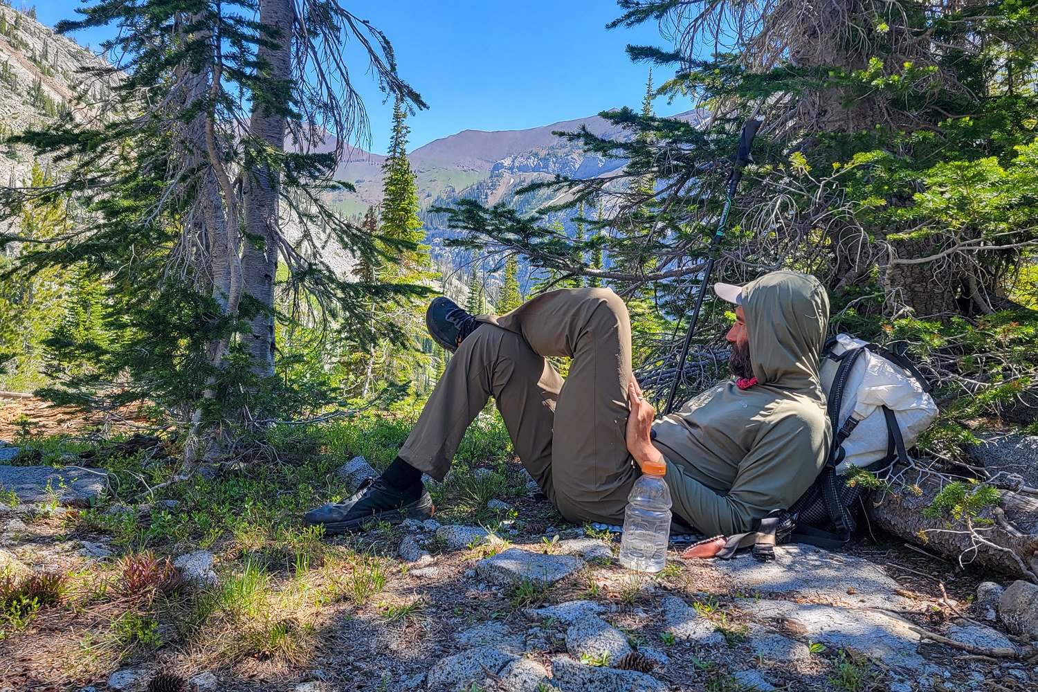 A hiker lounging against his backpack with his feet up, there's a mountain view in the background