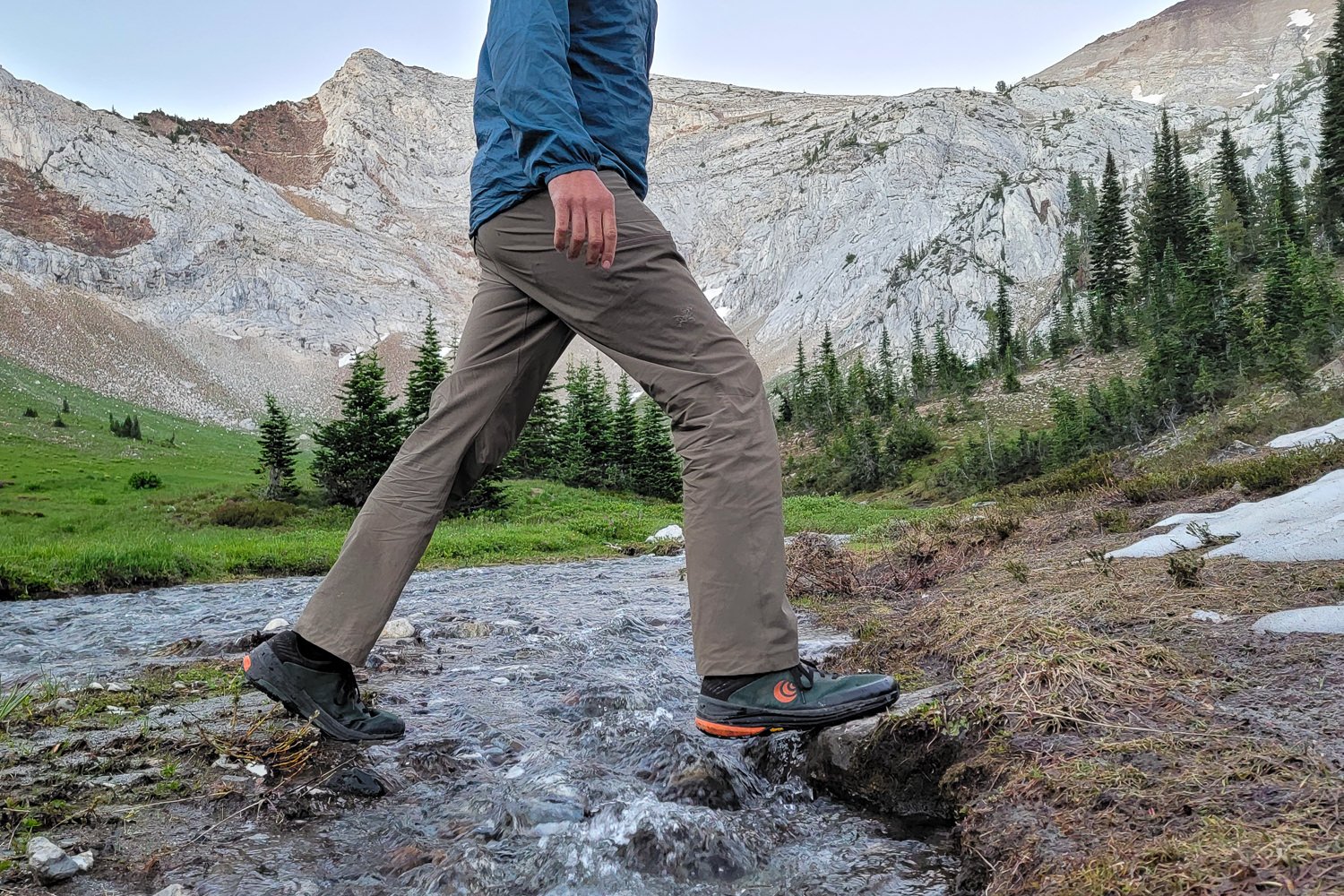 A hiker walking across a stream in Topo Ultraventure shoes with mountains in the background