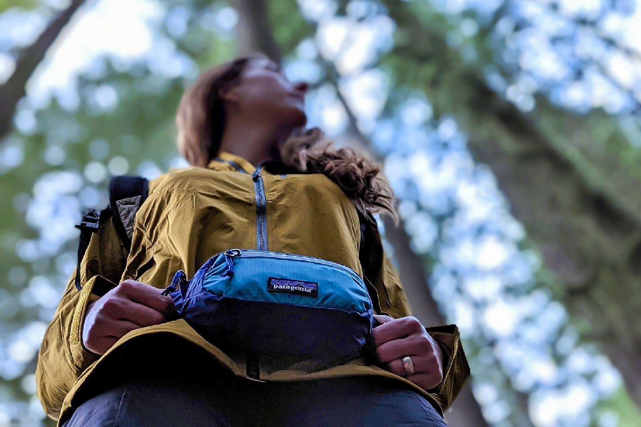 A view from below looking up at a hiker wearing the Patagonia Black Hole Mini Hip Pack in a forest