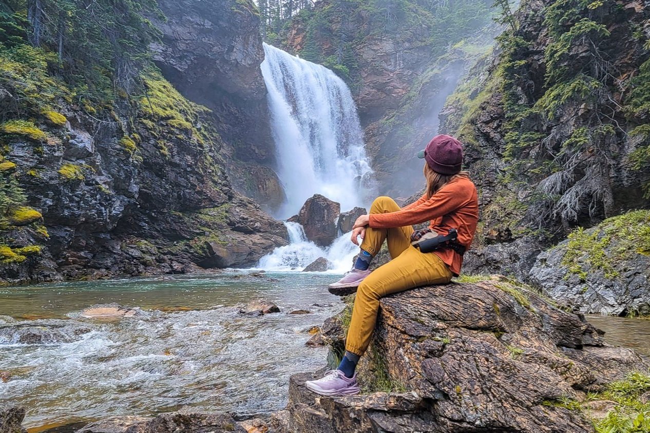 A hiker in the prAna Halle E-Waist Jogger II hiking pants in front of a mossy waterfall