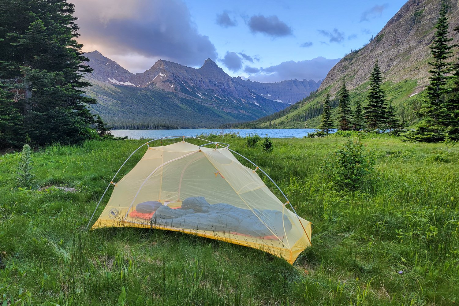 The Big Agnes Tiger Wall set up in a lush campsite with a lake mountain and moody sky in the background
