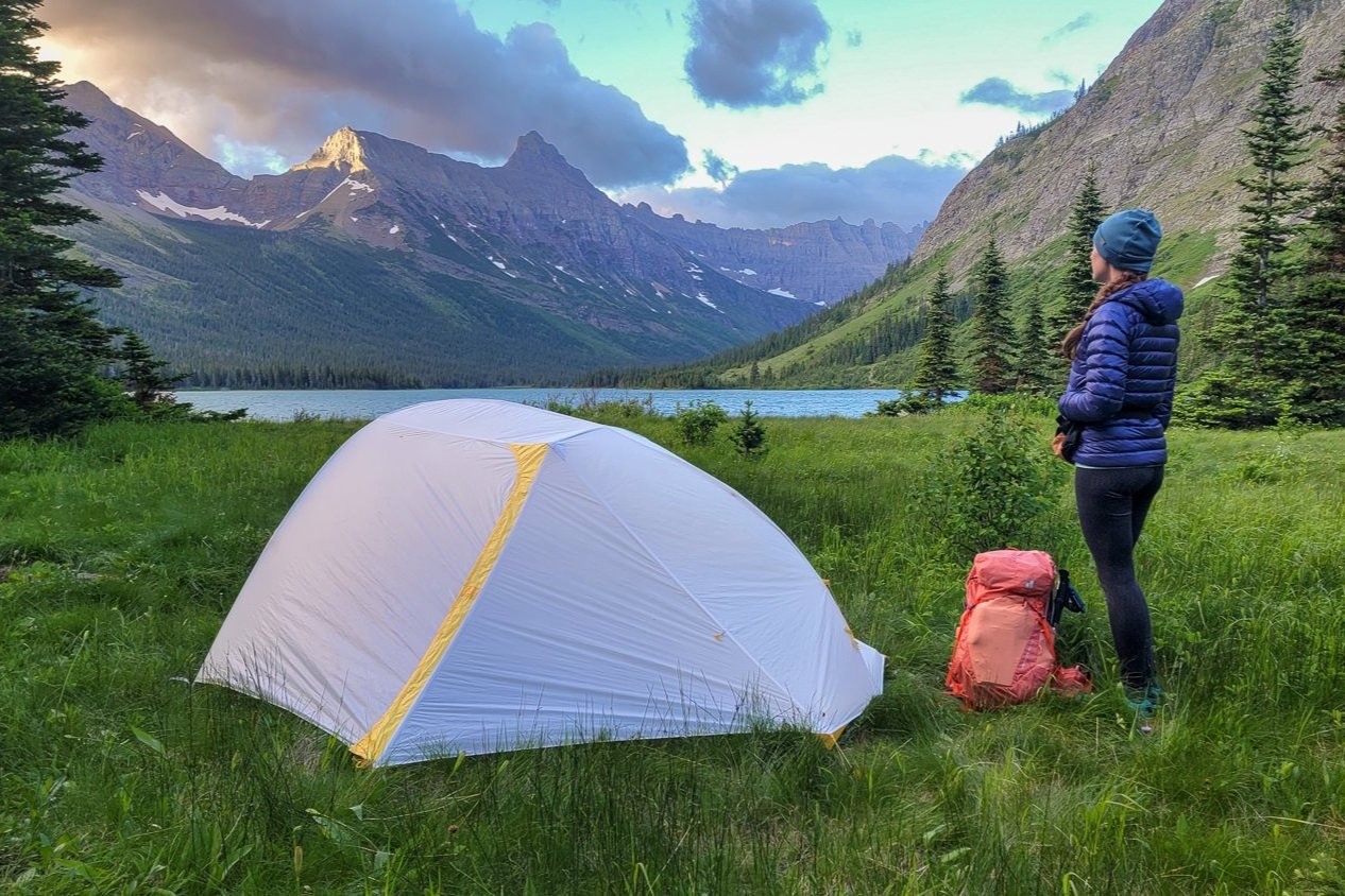 A backpacker standing by the Big Agnes Tiger Wall UL2 with sunrise mountains in the background