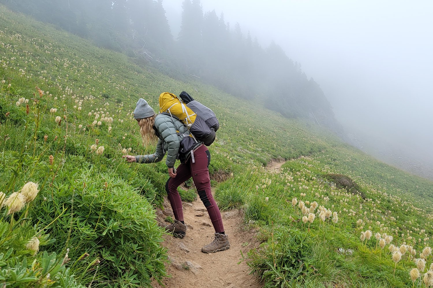 A hiker wearing leggings smelling a flower on a misty morning in the mountains