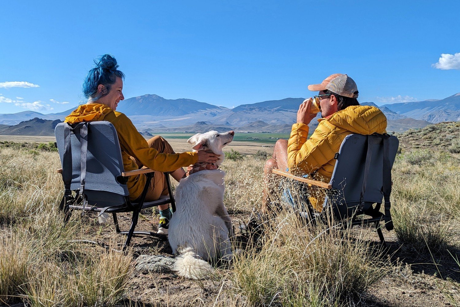 Two people sitting in the REI Outward Padded Low Chairs with their dog next to them in a beautiful desert scene