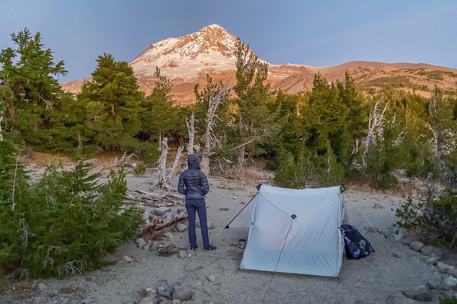 A hiker standing next to the Lunar Duo in front of a mountain peak at sunset