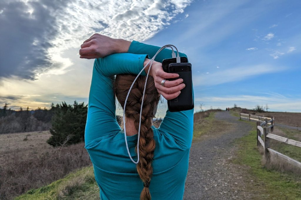 A runner facing away from the camera with her arms extended overhead holding the Inui 2000 PD Power Bank in her hand