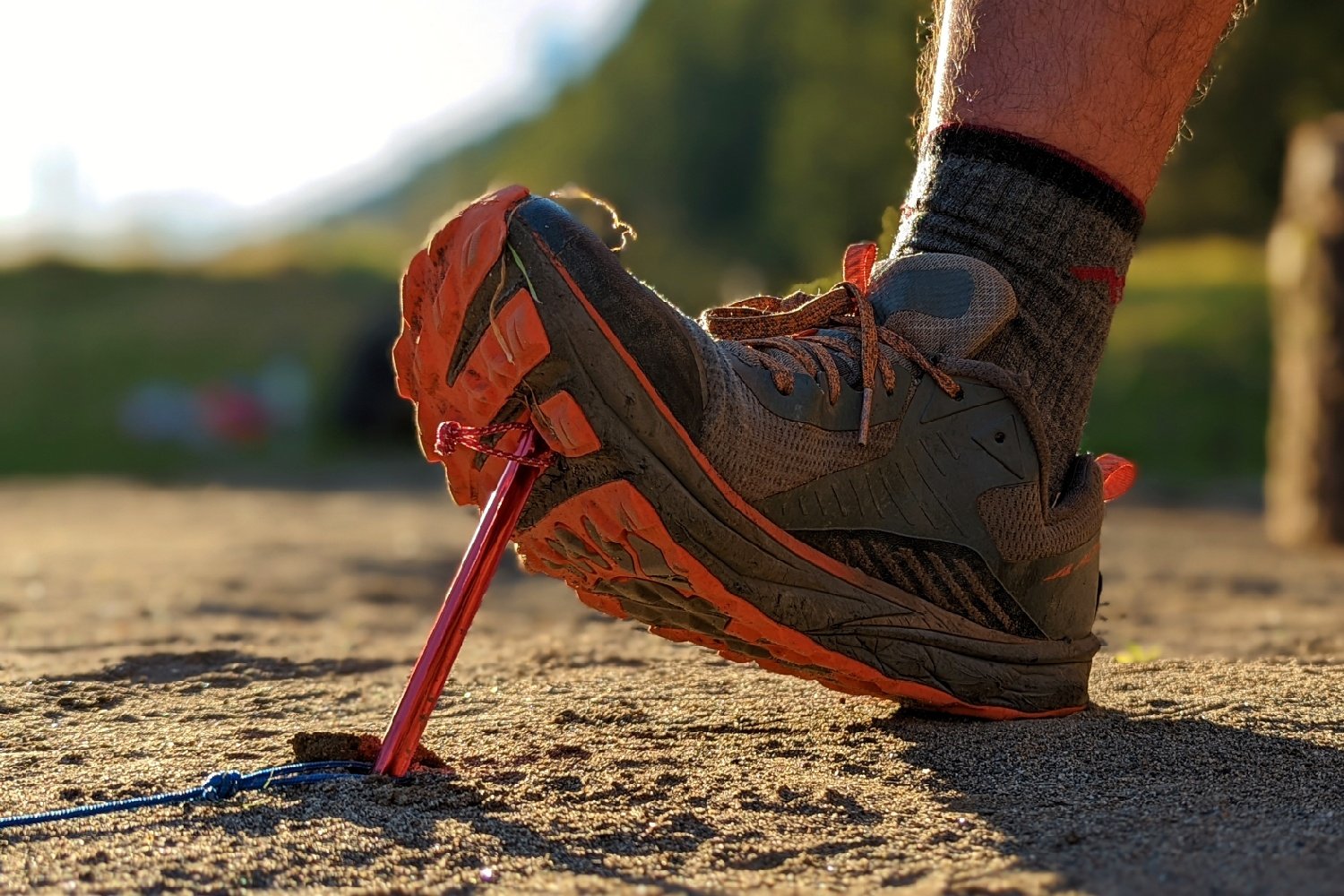 Closeup of a hiker's foot pressing an MSR Ground Hog tent stake into the dirt