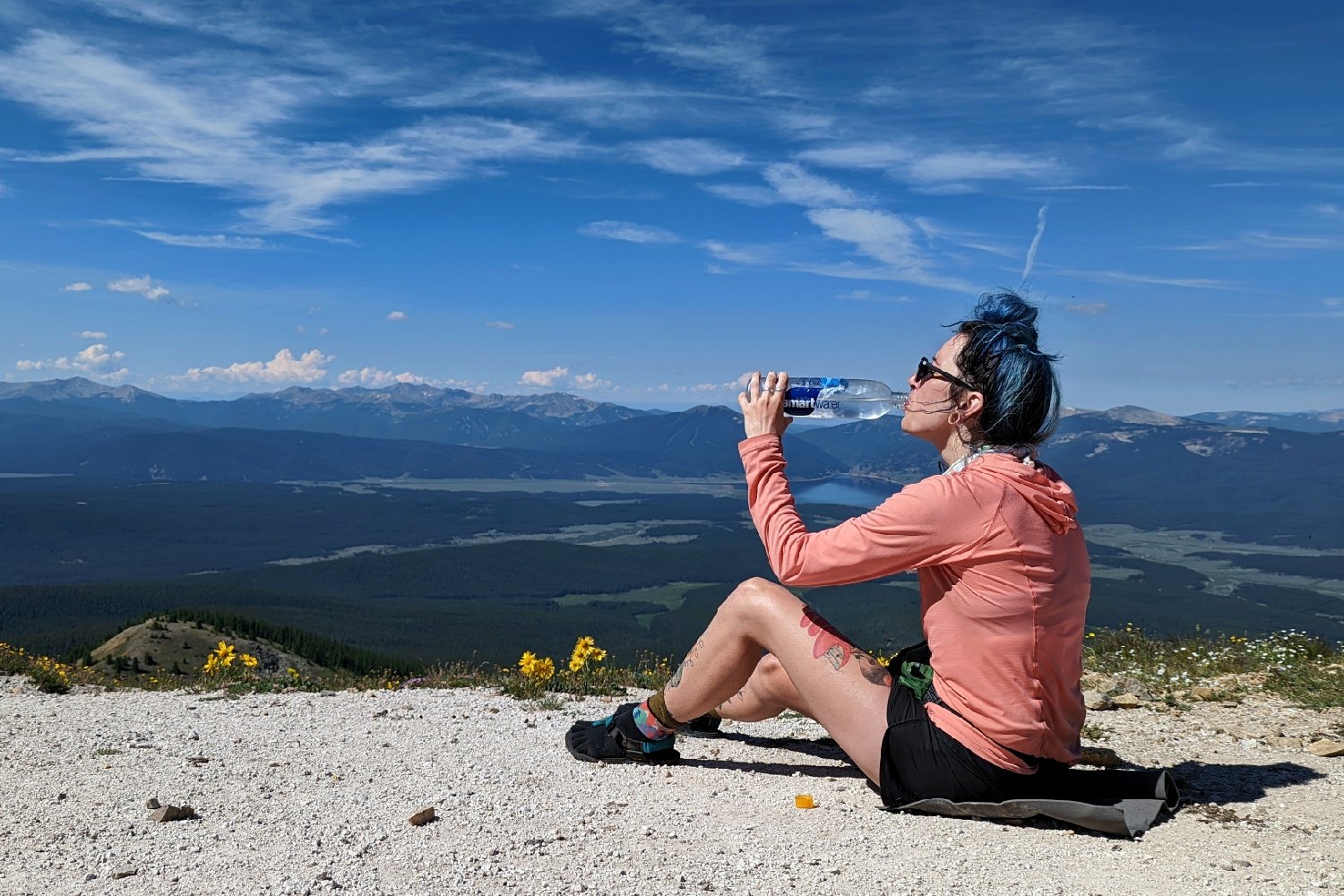 A hiker sitting on a mountain pass drinking out of a smartwater bottle