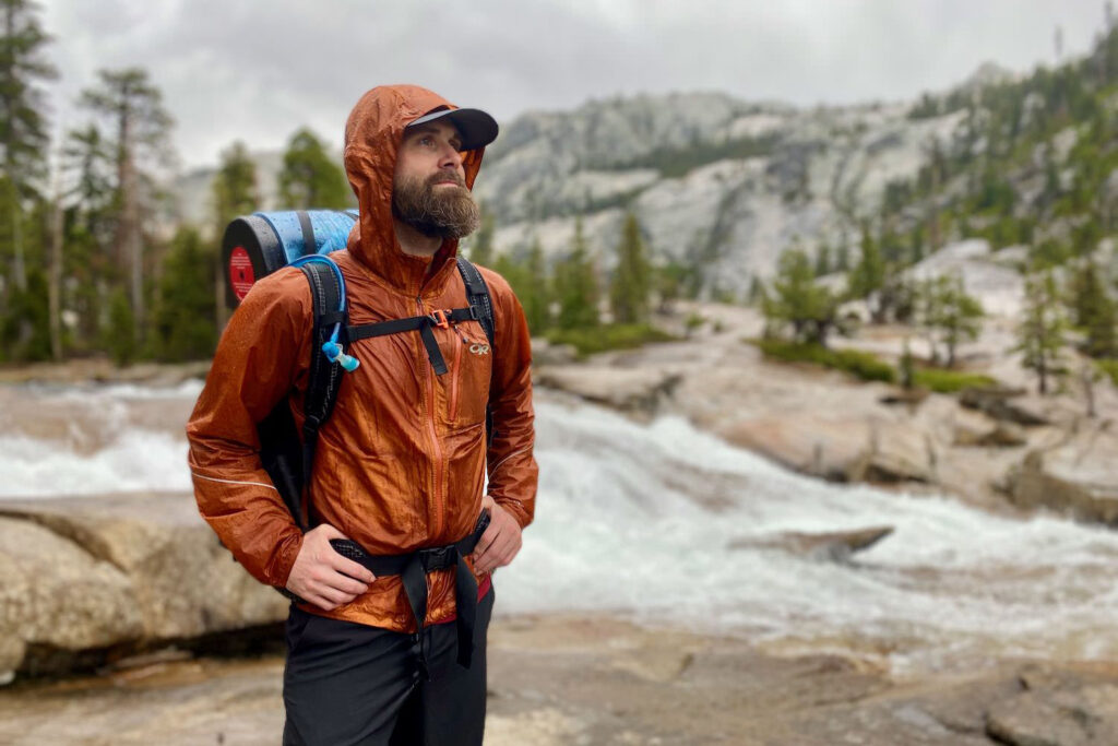 A backpacker wearing an orange Outdoor Research Helium rain jacket in Yosemite National Park