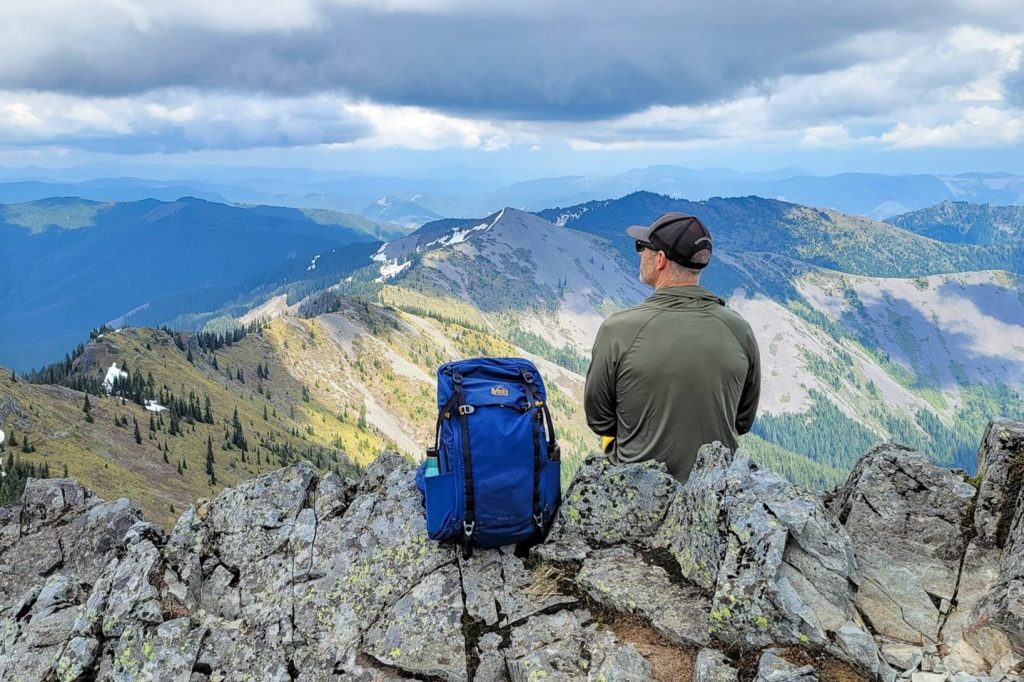 A hiker sitting next to the REI Trail 25 daypack on a mountain ridge