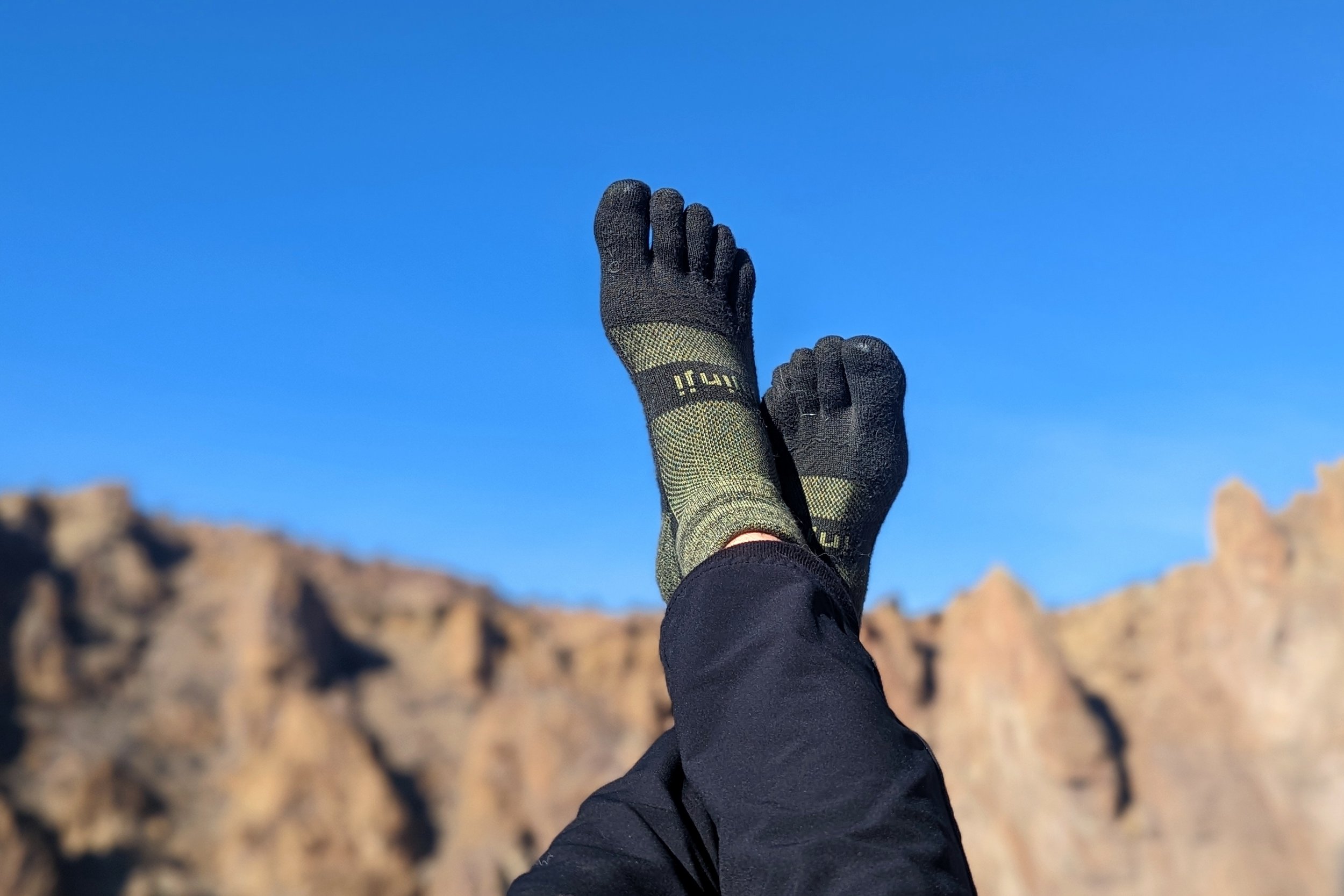 Photo of a person's feet with socks on a background of sky and a mountain range. The socks are toe socks