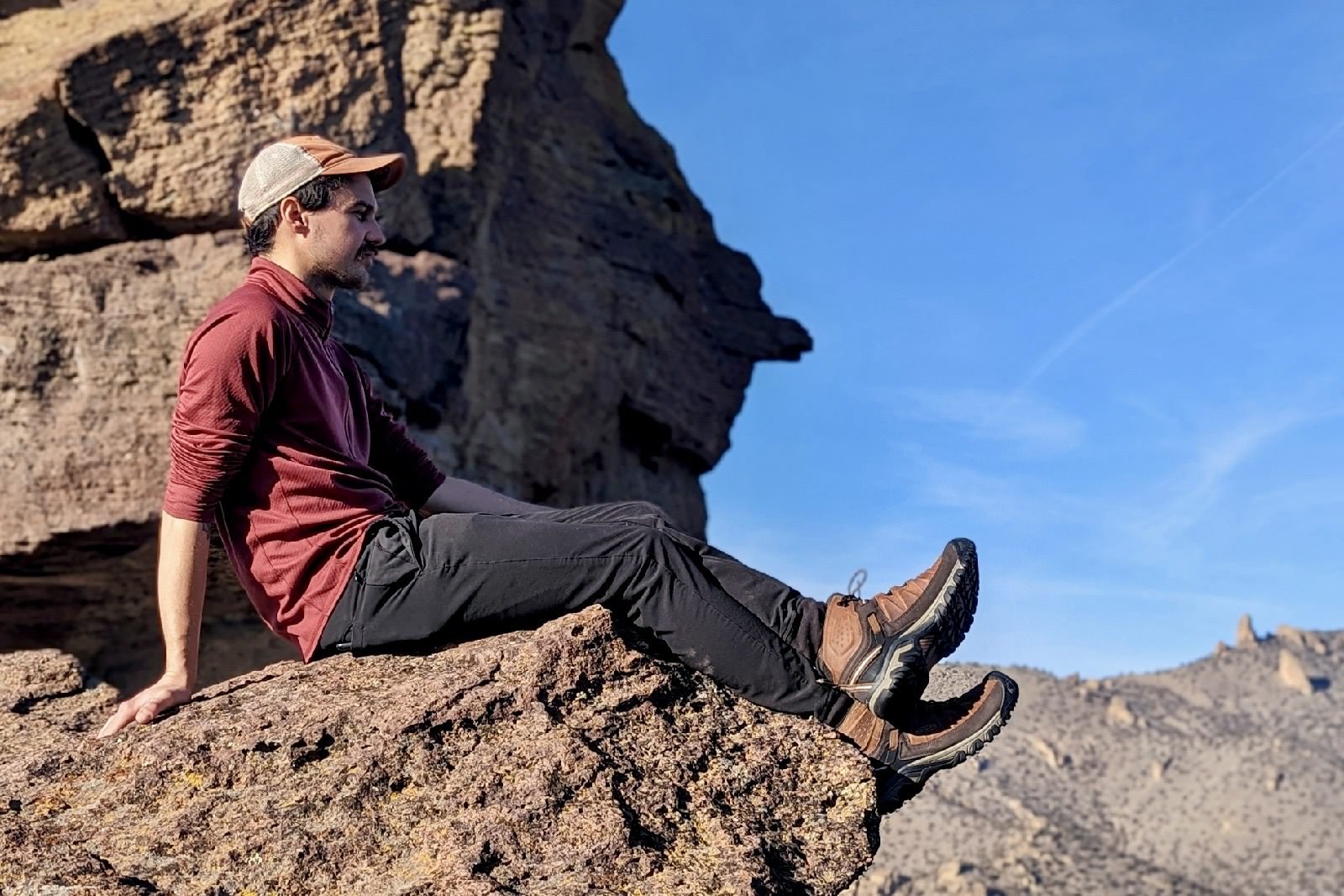 A hiker sitting on a ledge looking out over a mountain view with hiking boots on