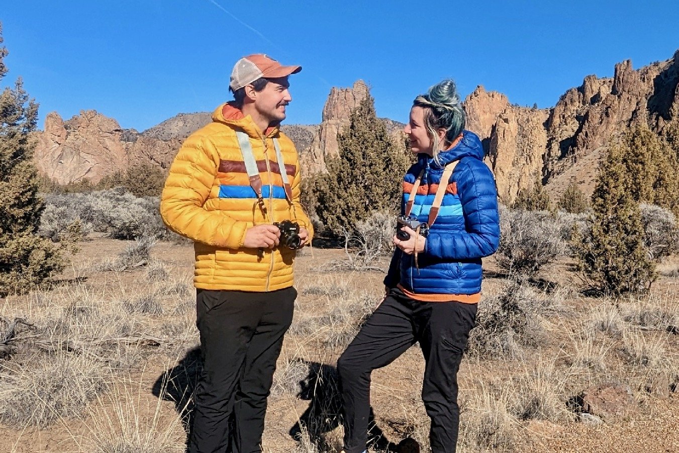 Two hikers wearing Cotopaxi Fuego Down jackets in a mountainous desert landscape