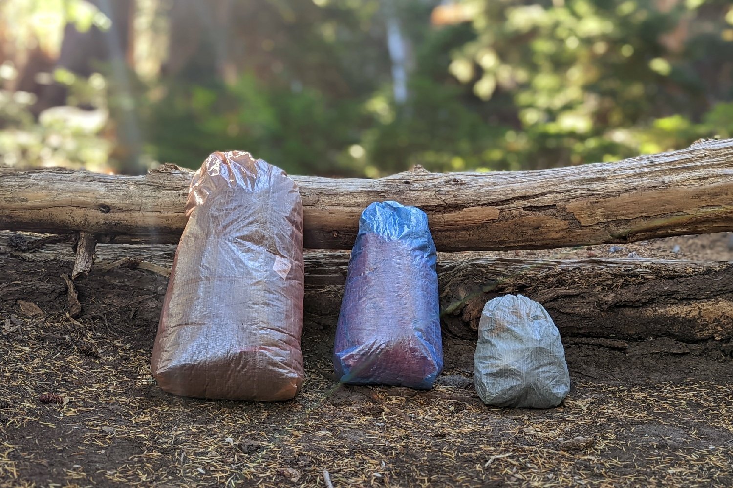 Three Zpacks Drawstring Stuff Sacks of different sizes and colors in front of a log in a forest