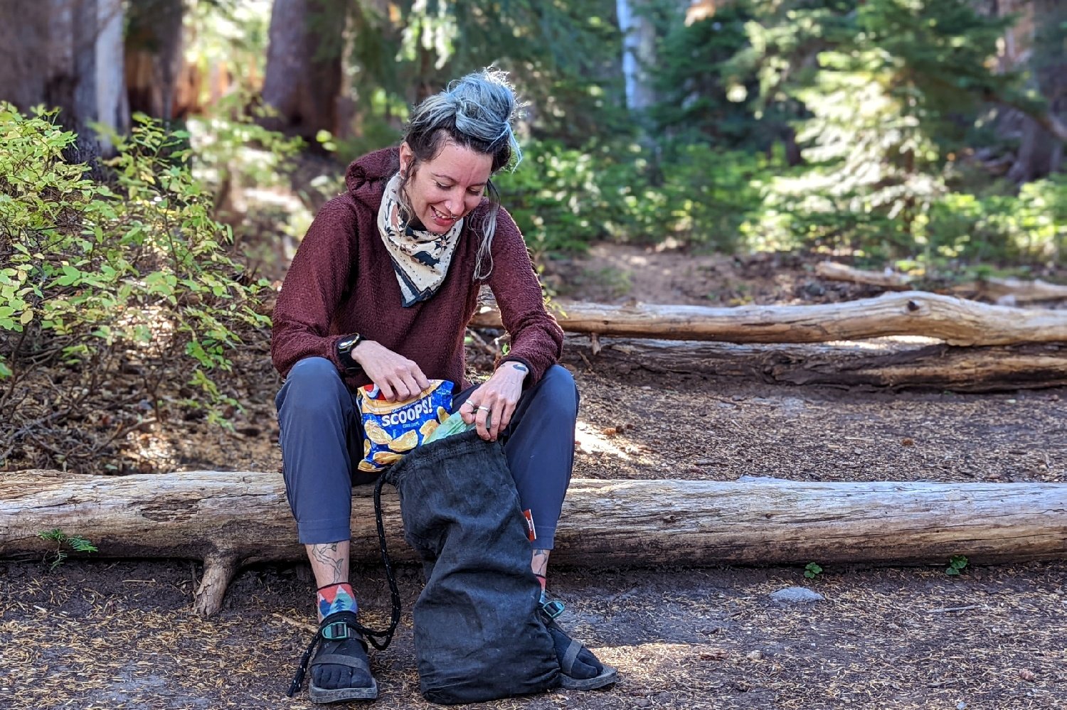 A hiker sitting on a log pulling a bag of Fritos out of an Ursack Major