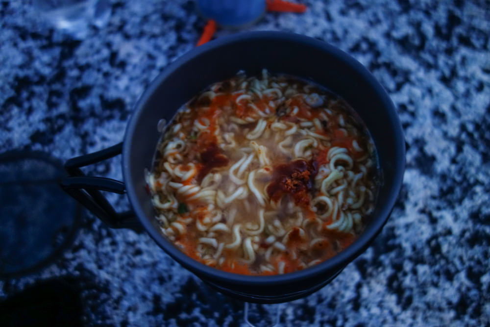 Top-down view of Top Ramen in a backpacking pot with spices.