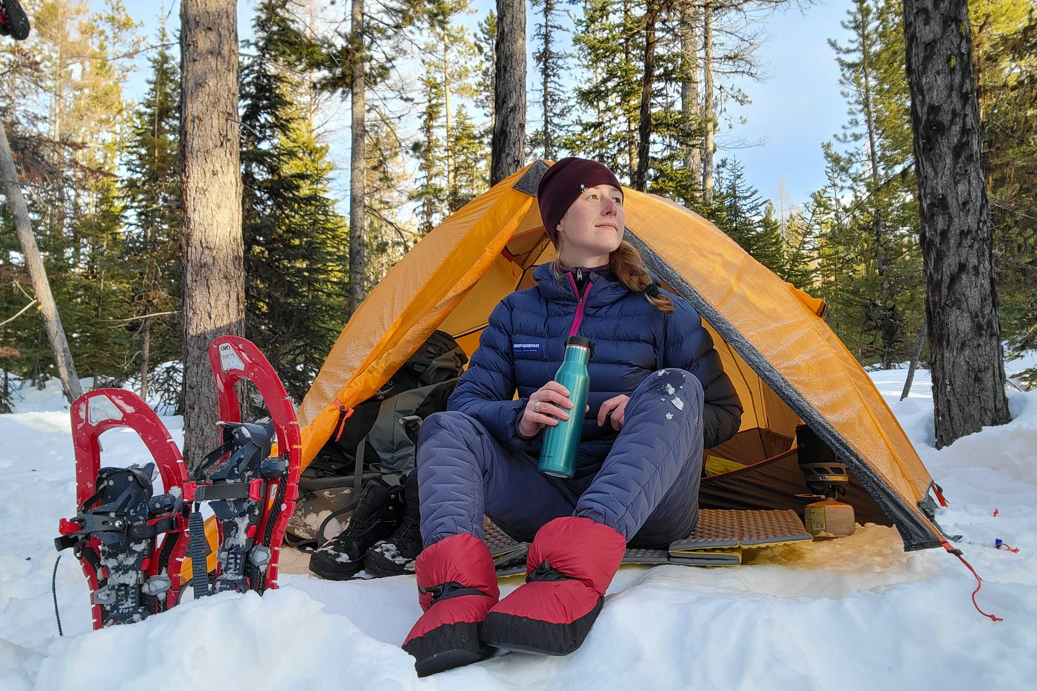 A hiker sitting in the entry of the NEMO Kunai Tent with some snowshoes next to them