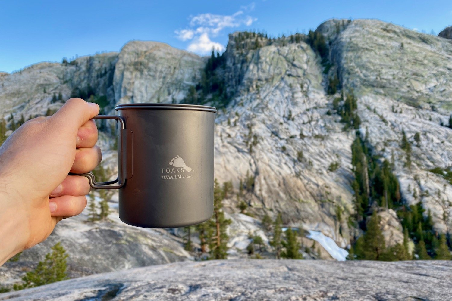 Closeup of a hand holding the TOAKS Titanium 750ml backpacking pot in front of granite mountains in Yosemite National Park