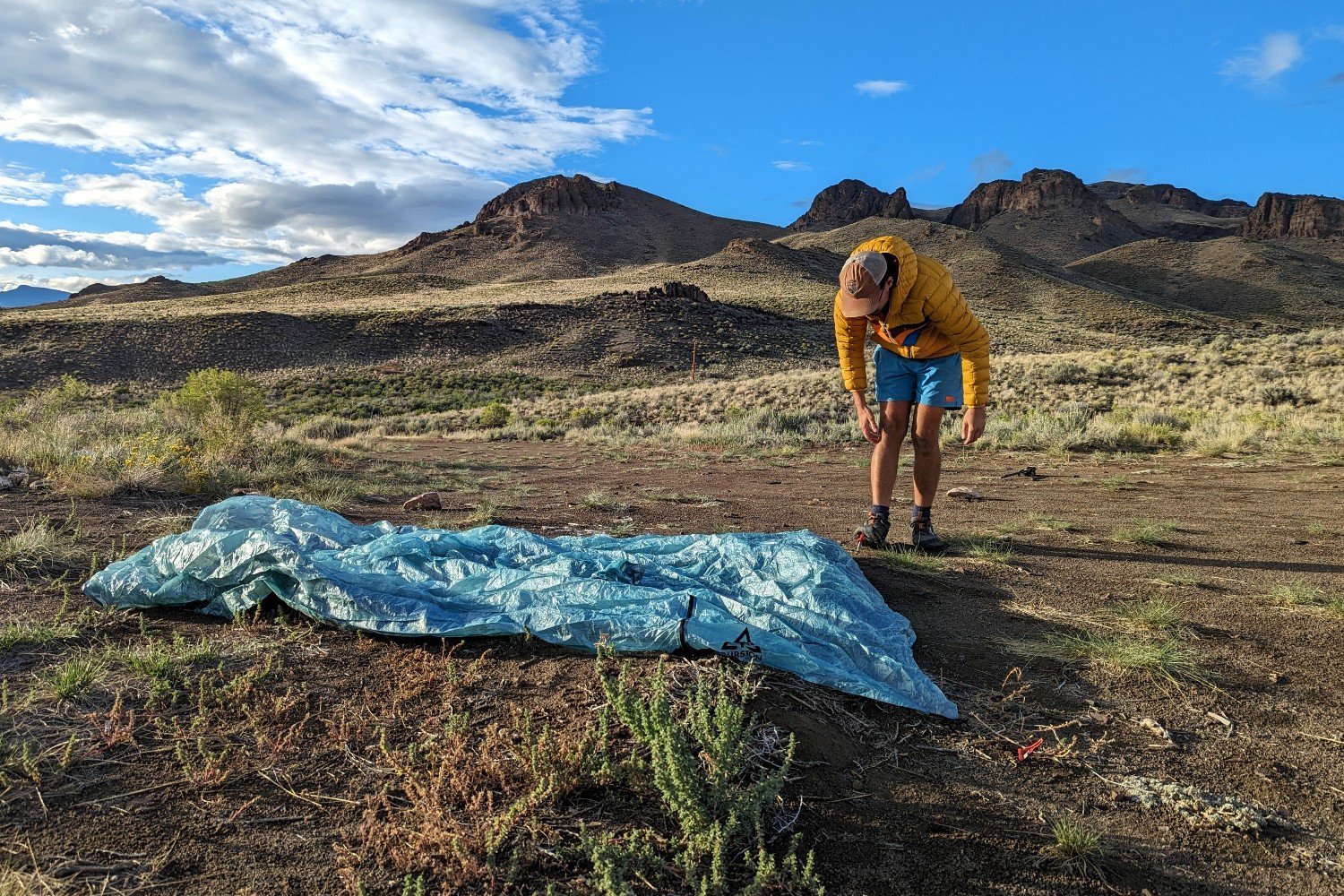 The Durston X-Mid 2 Pro tent laid on the ground and a hiker staking out the sides. There are mountains and dark clouds in the background