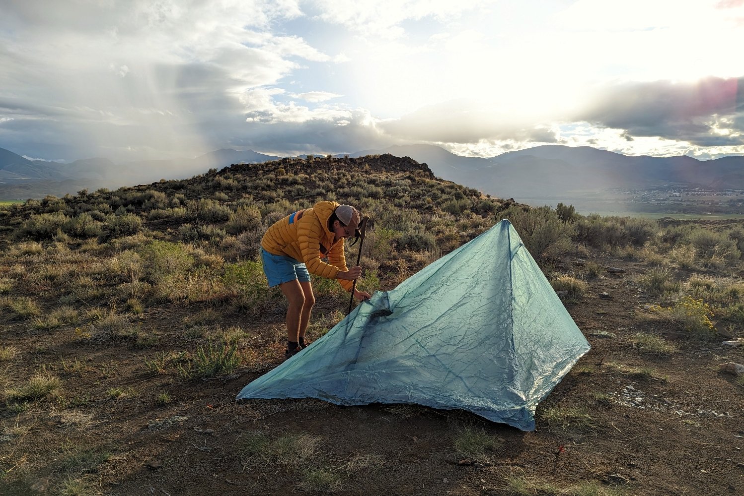 A hiker setting up the Durston X-Mid 2 Pro tent in a brushy desert campsite as a light rain approaches