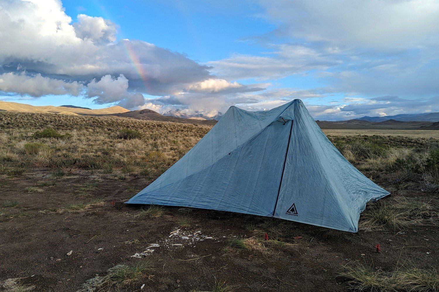The Durston X-Mid 2 Pro tent set up in a desert campsite with mountains in the background. There are some rain clouds and a rainbow in the background