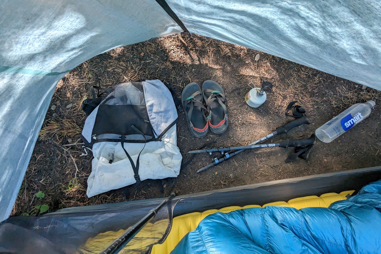 A backpack, some sandals, collapsed trekking poles, a backpacking stove, and a smartwater bottle laid out in the vestibule of the Durston X-Mid 2 Pro tent
